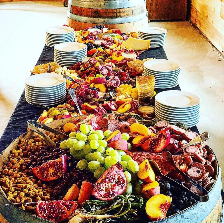 A long catering table set with charcuterie, cheeses, fresh fruit and nuts on wine barrels